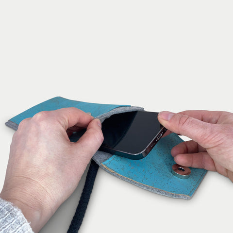 Person, die ein Motorola Moto G55 in eine stilvolle hellgraue und blaue Filztasche mit Schulterriemen steckt.