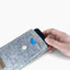 Ein Motorola Moto G56 wird von Hand aus einer stilvollen hellgrauen Handytasche mit Knopfverschluss gezogen.